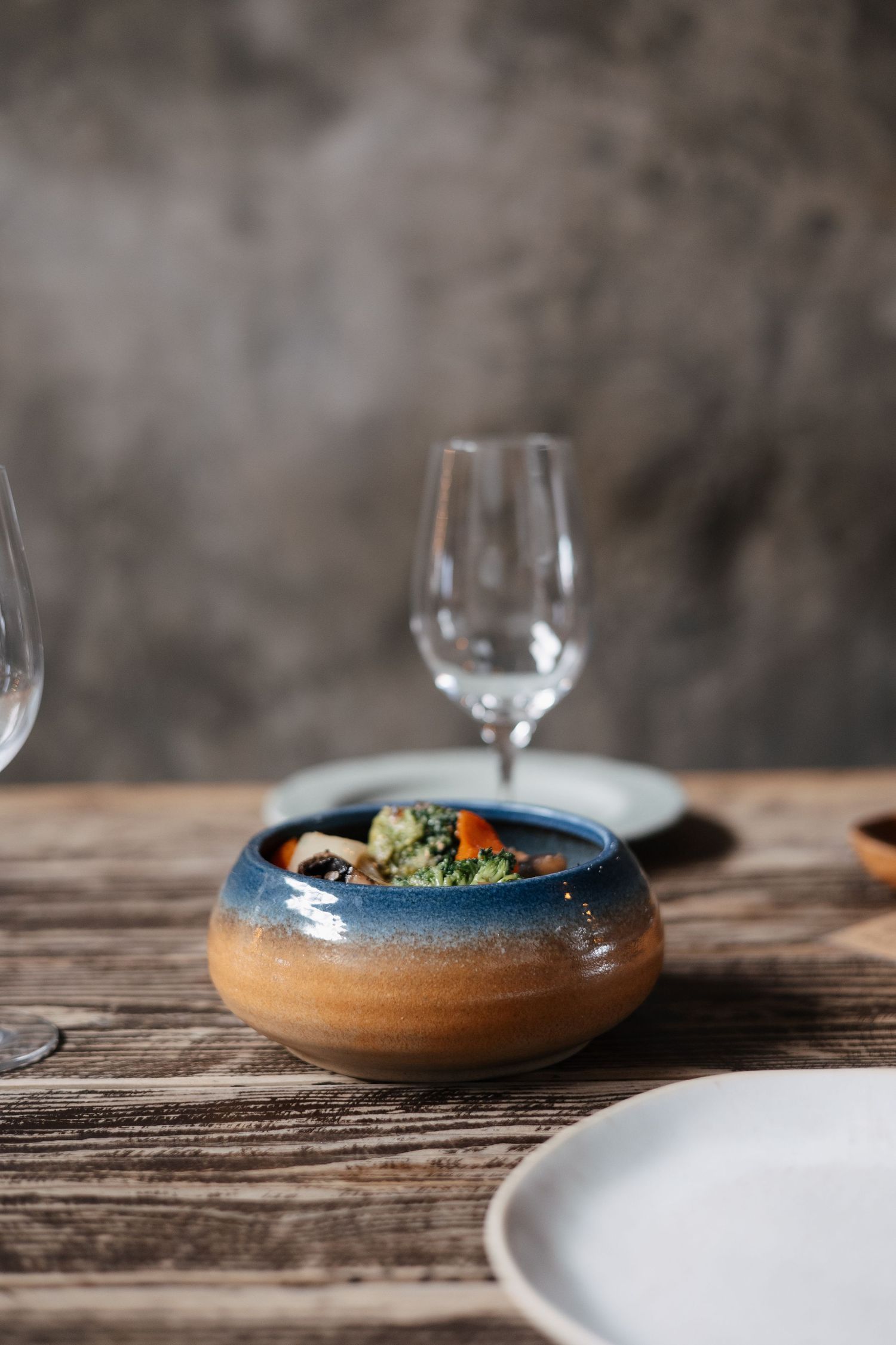 Elegant ceramic bowls and wine glasses arranged on a weathered wooden table.
