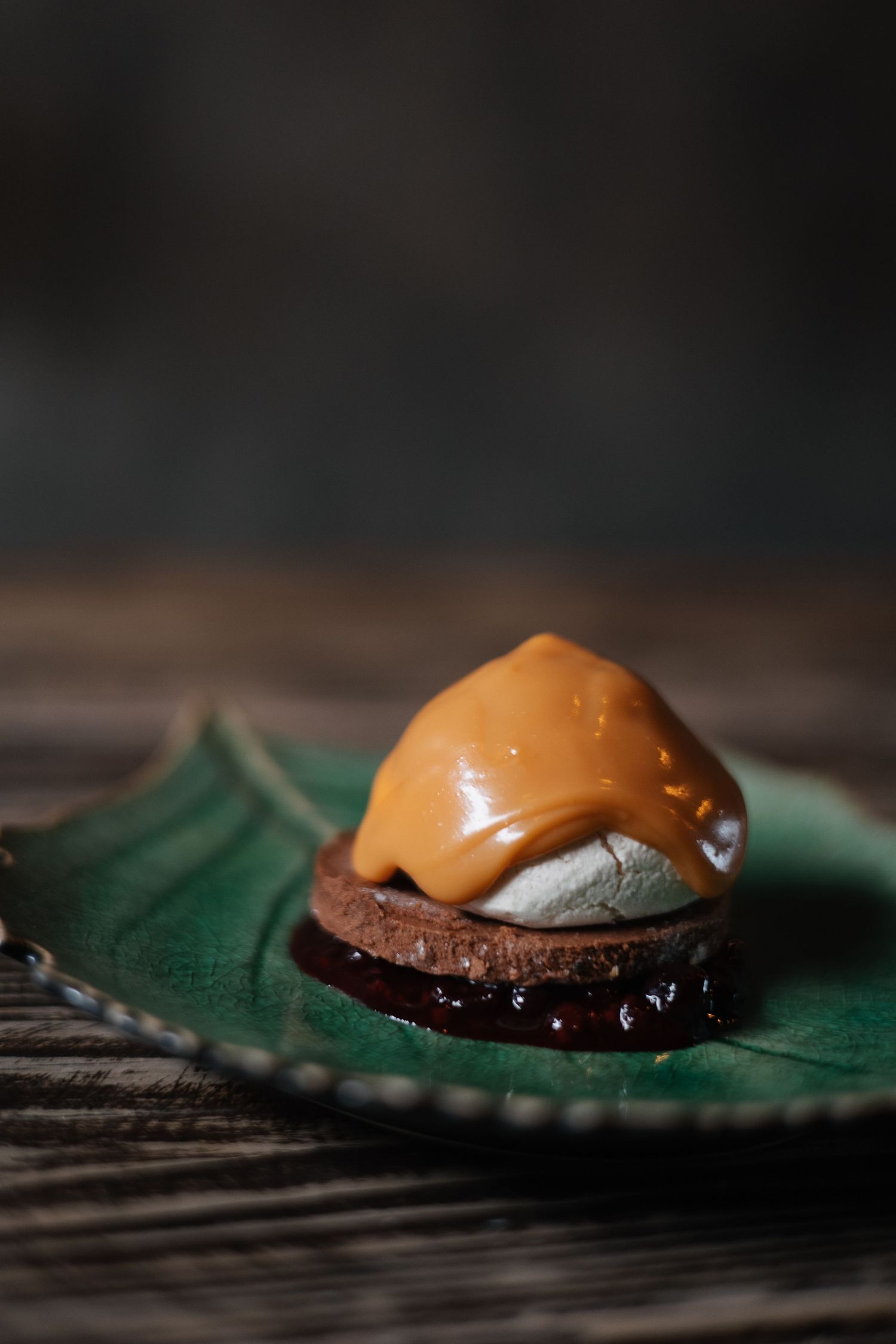 Close-up of a caramel-colored dessert dome on a dark plate with green garnish.