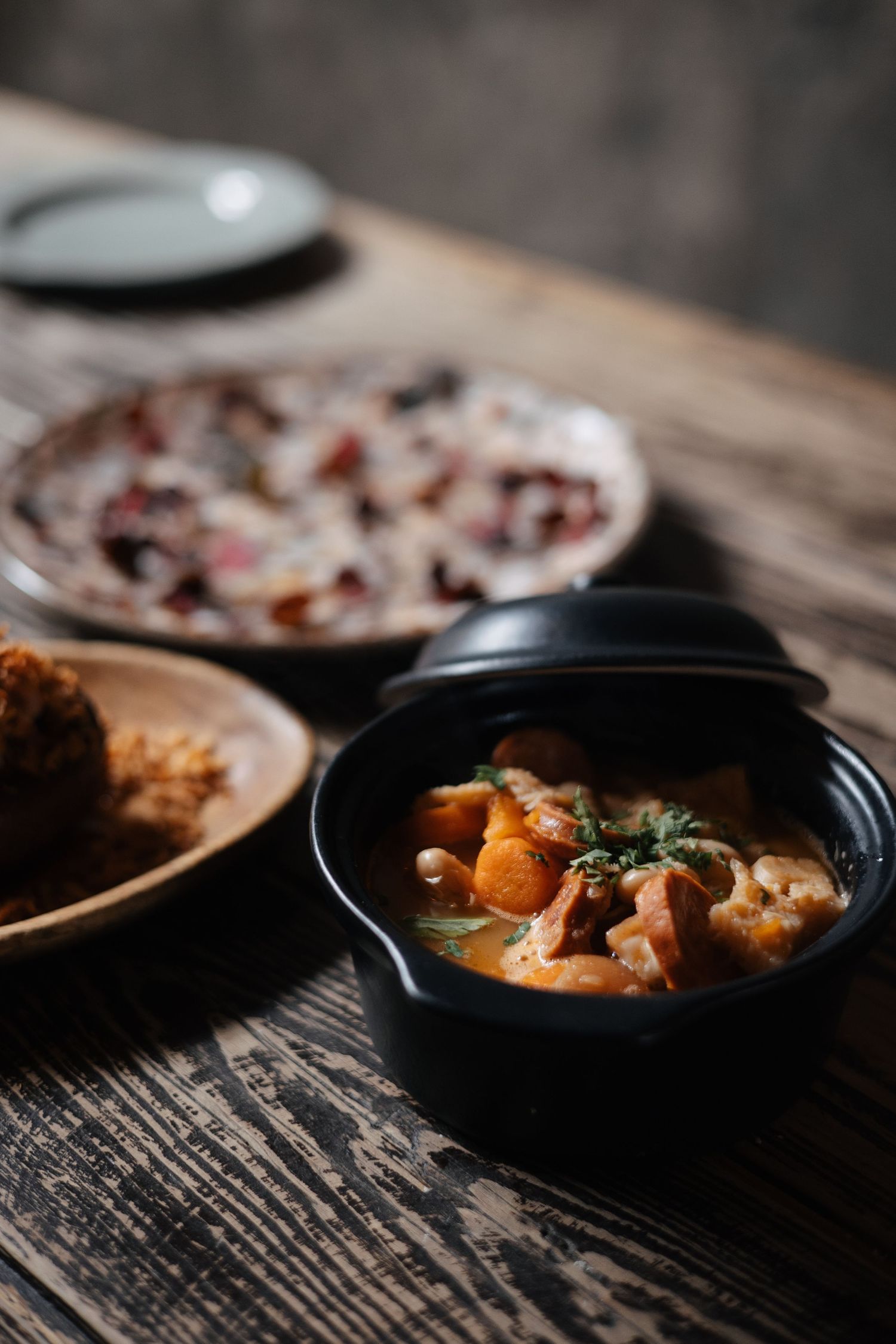 Steaming curry dish served in a black bowl on a textured wooden table.