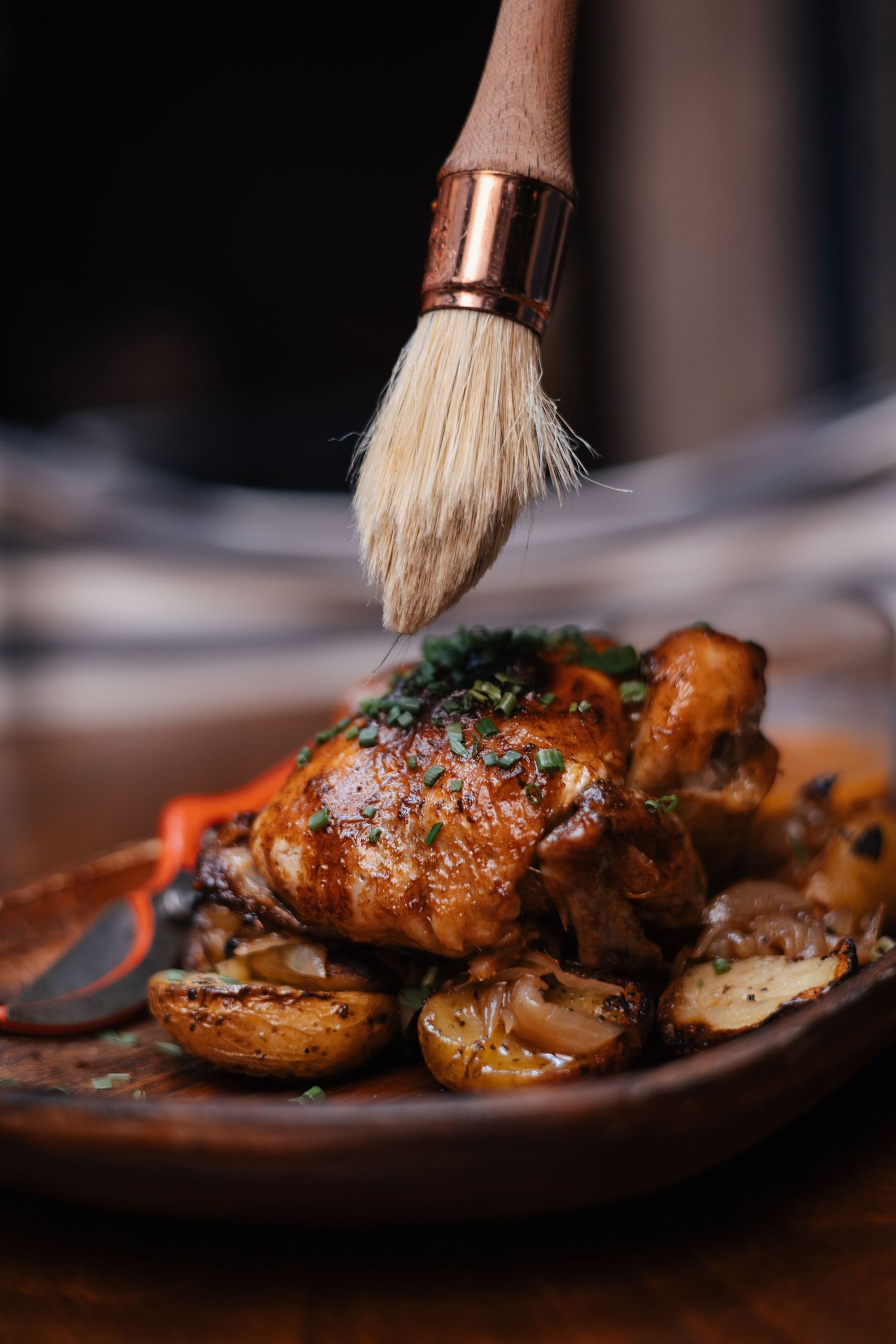Glazed chicken or poultry dish being brushed with sauce on a rustic plate.