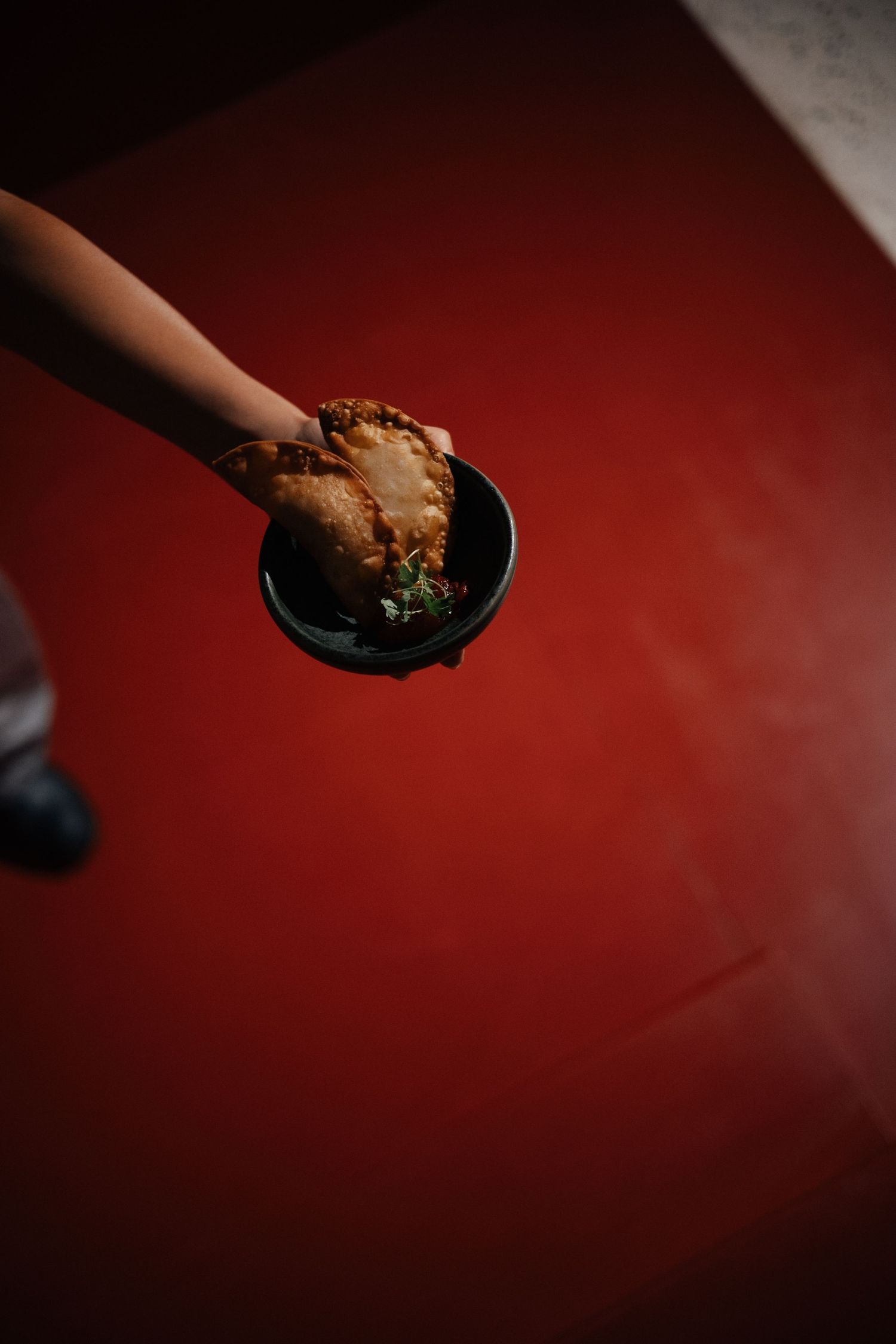 Hand serving food on a black plate against a deep red background.