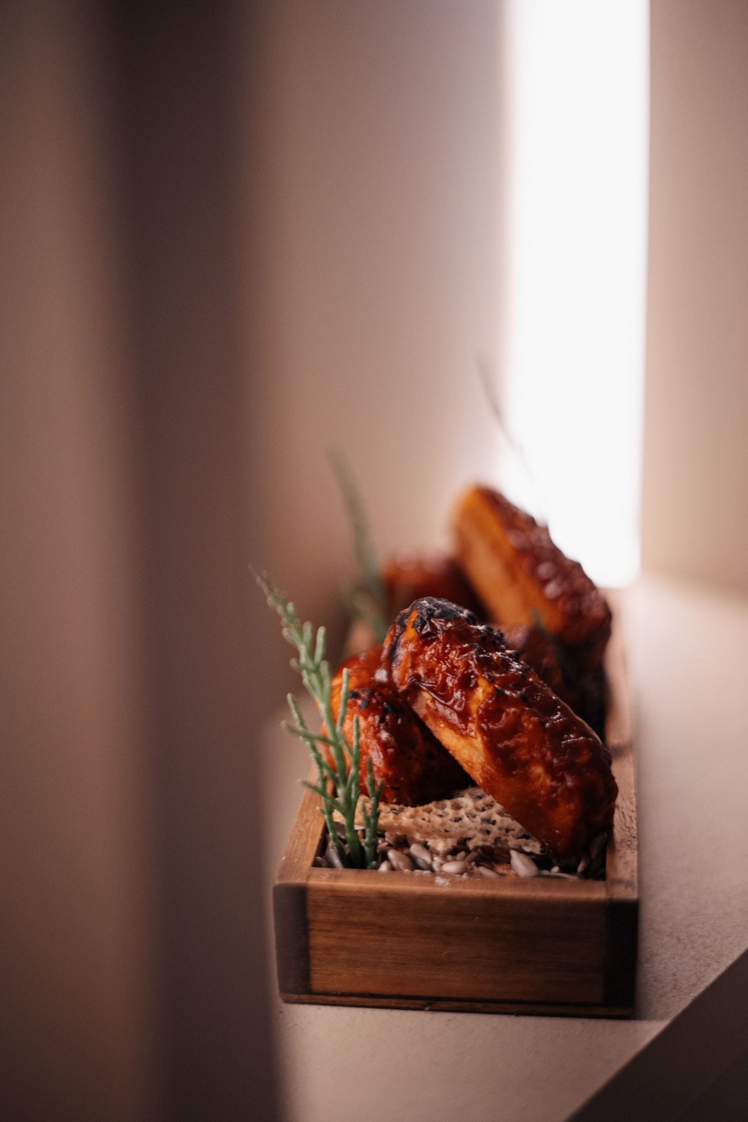 Roasted meat dish with herbs presented in a rustic wooden box under soft lighting.