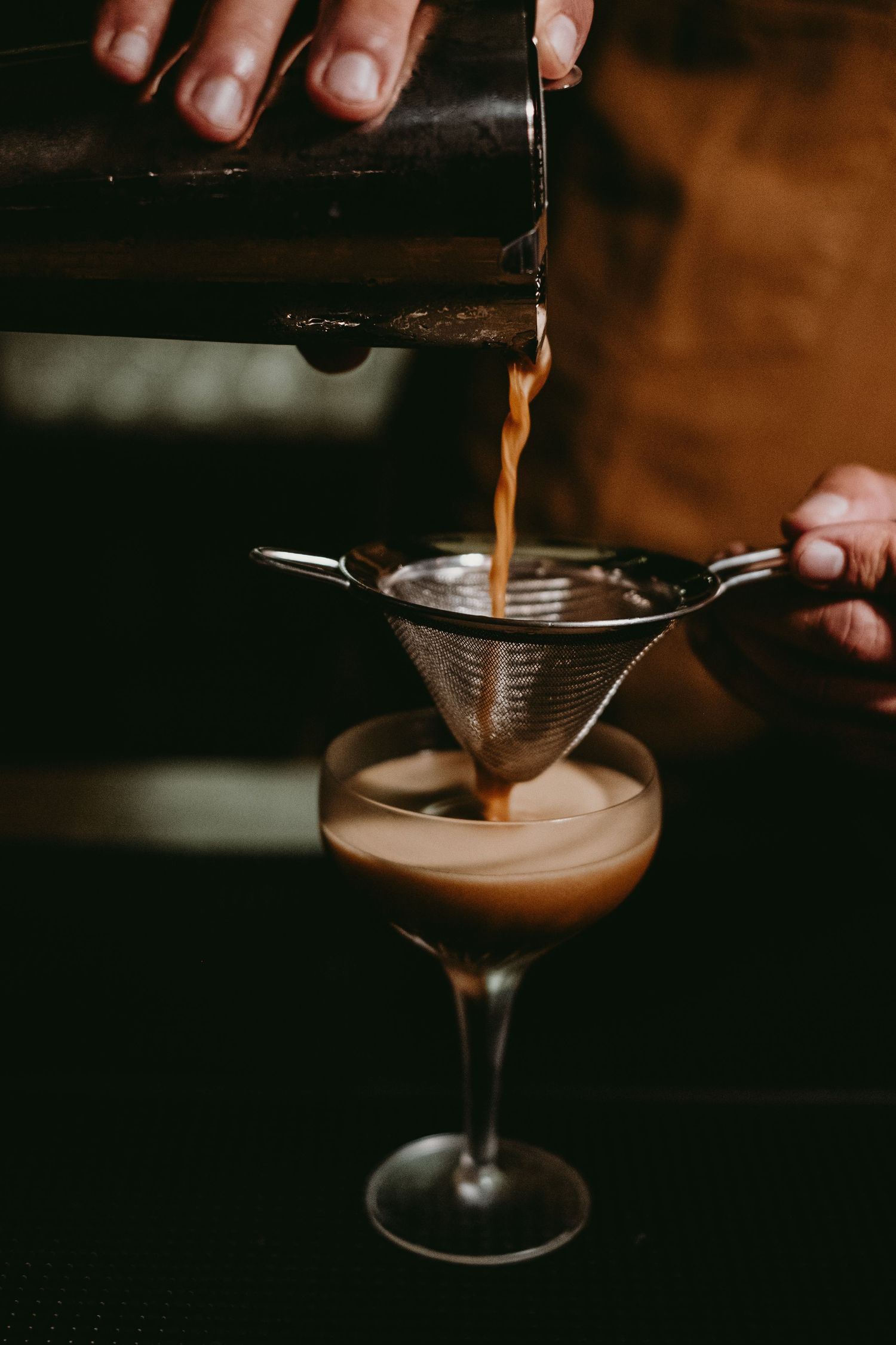 Bartender garnishing a creamy cocktail with coffee beans.