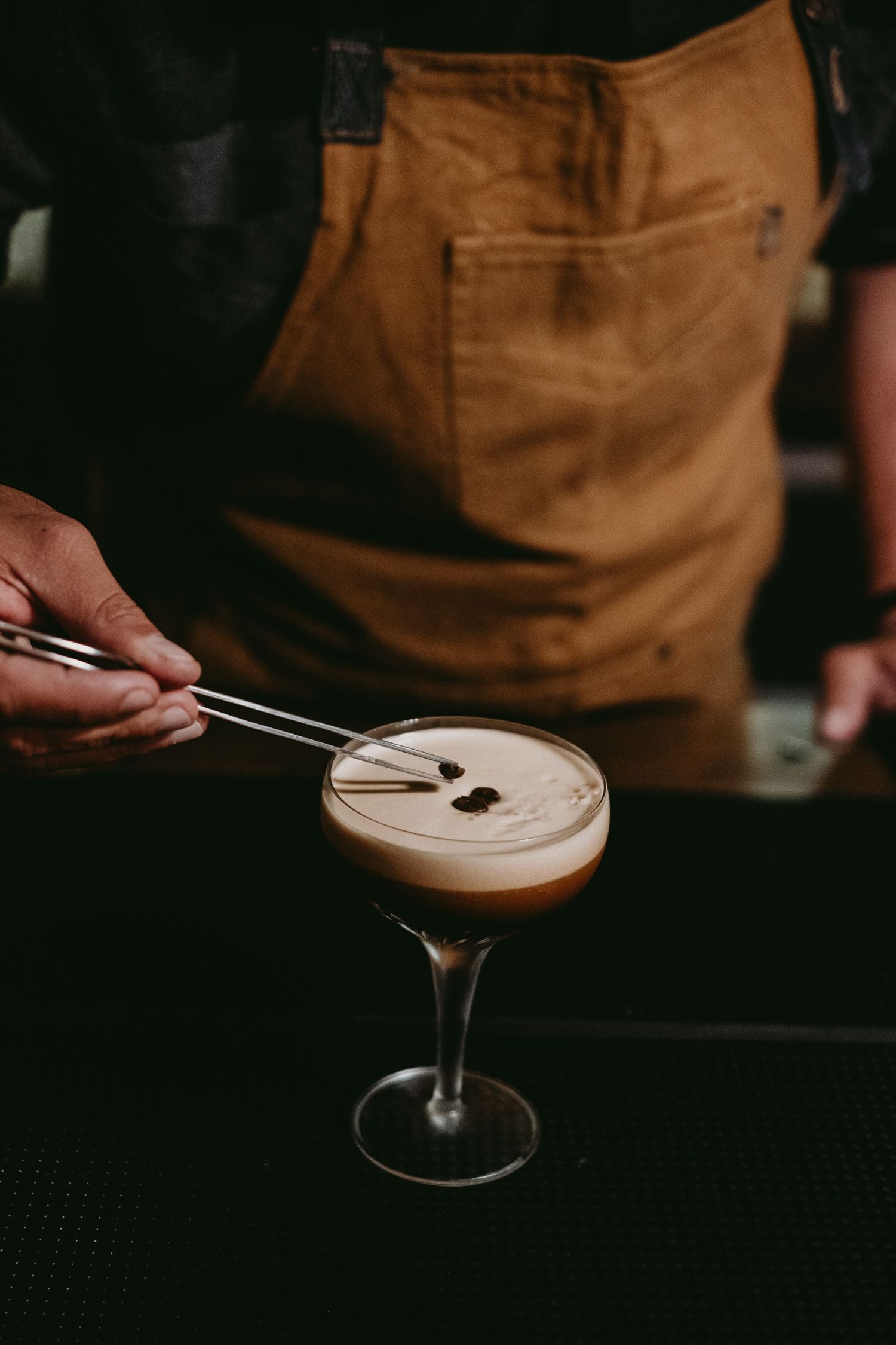 Bartender garnishing a creamy cocktail with coffee beans.