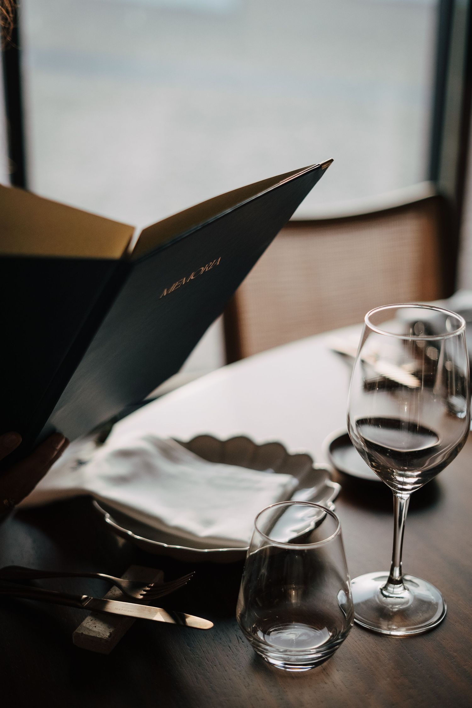 Wine glasses and menus on dark wooden table with natural window lighting.
