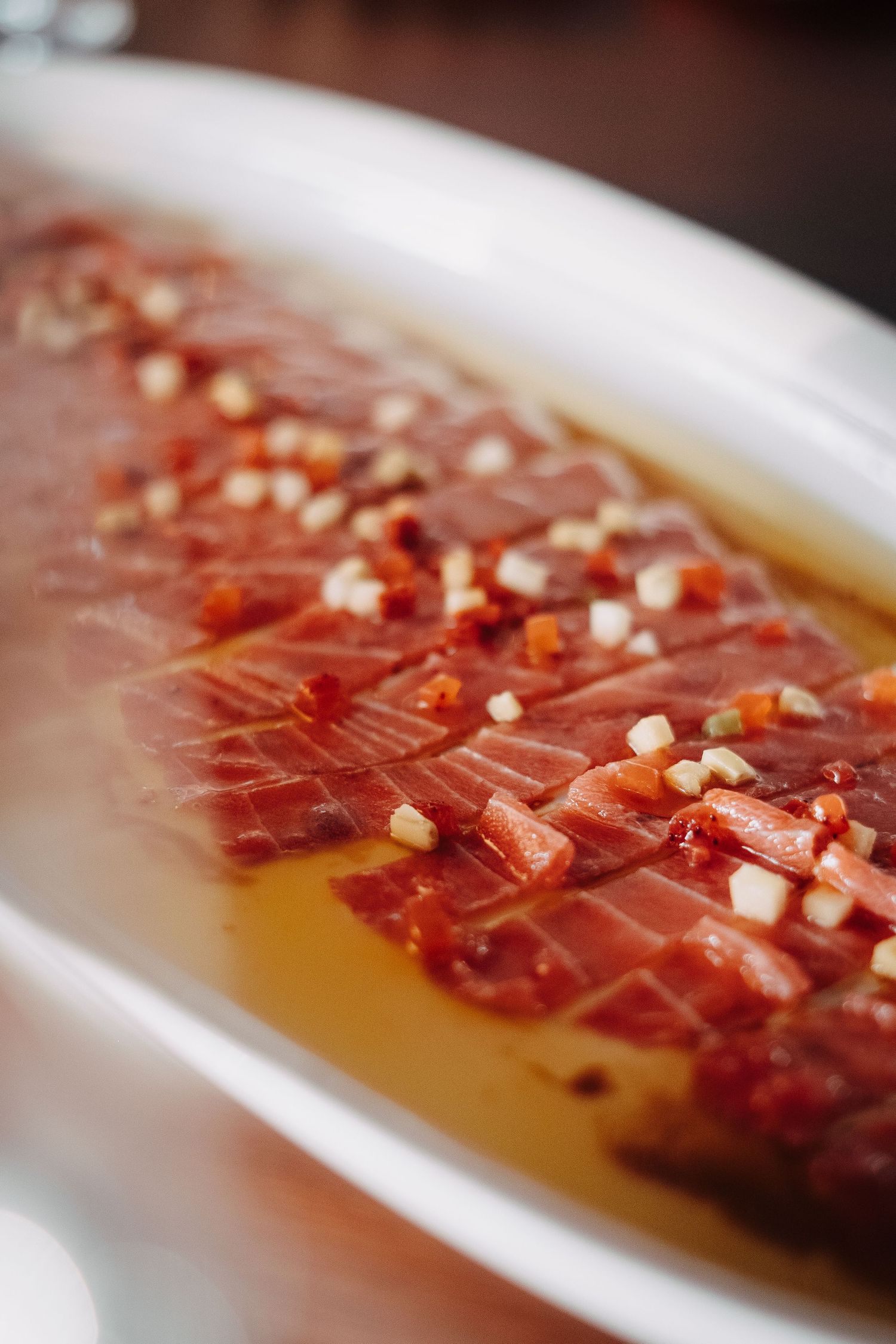 Close-up of delicate prosciutto slices arranged with olive oil and nuts on a white ceramic dish.