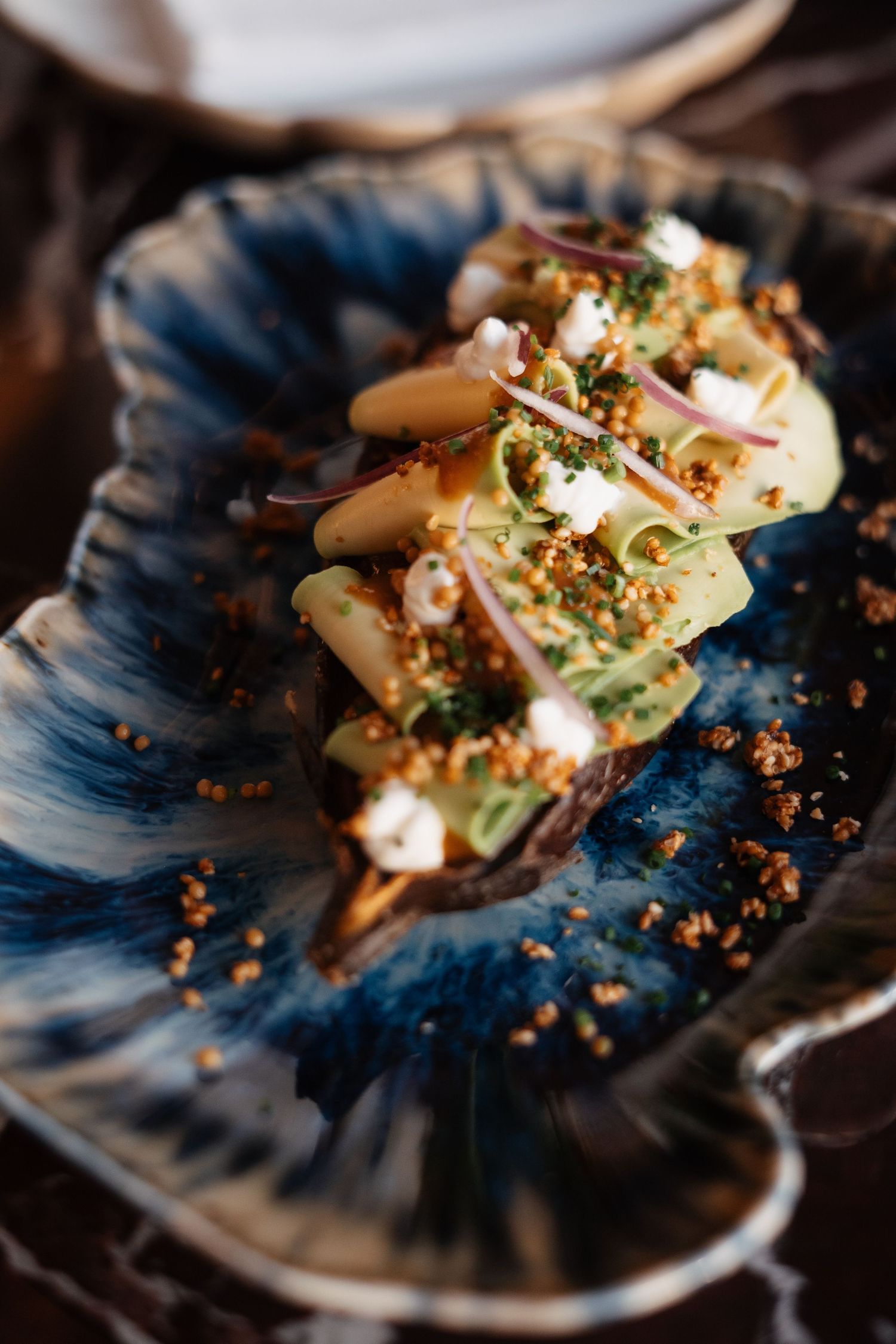Elegantly plated seafood dish with crumbs and microgreens on a blue ceramic plate.