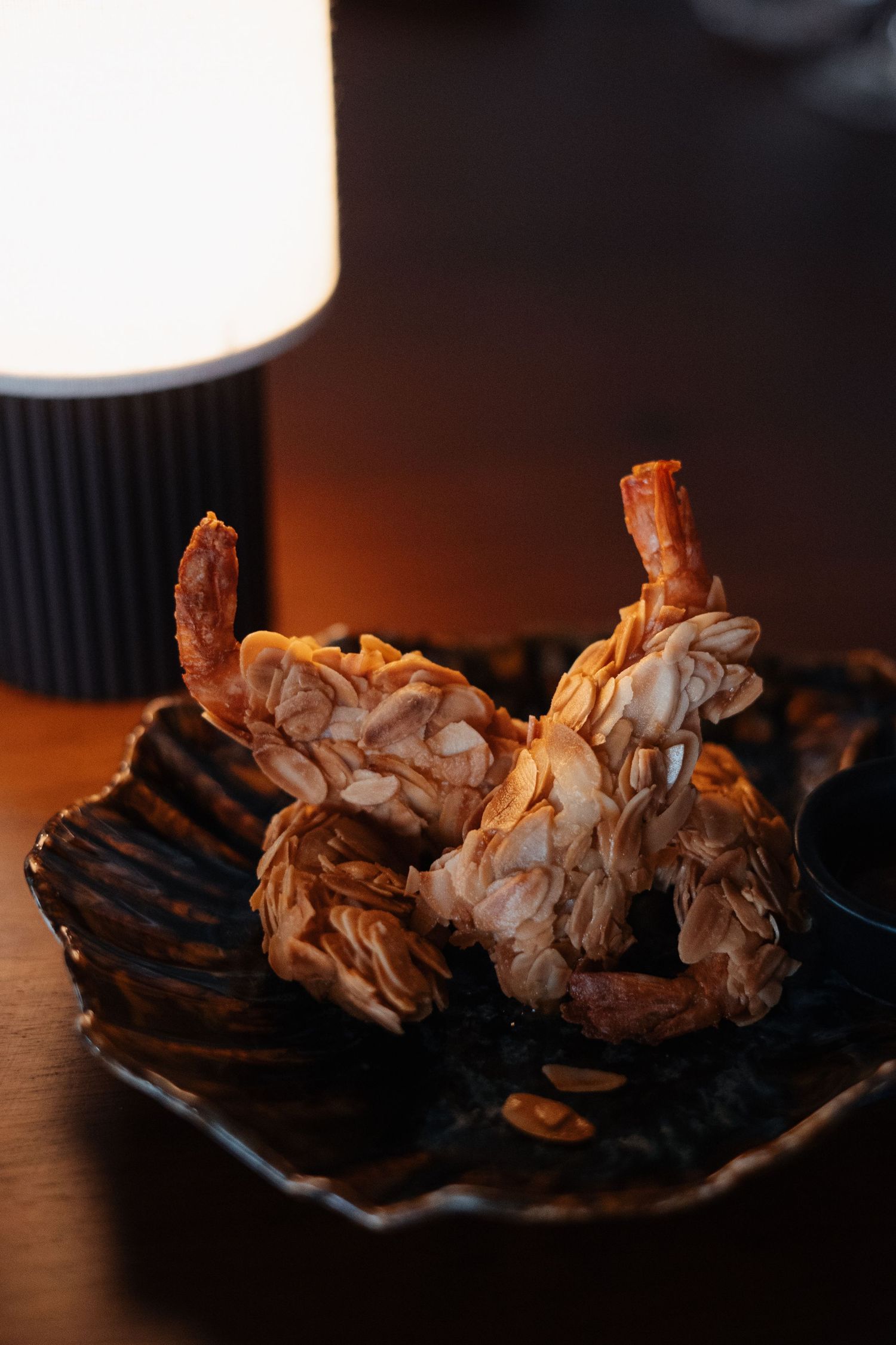 Grilled or roasted shrimp arranged on a dark textured plate in moody lighting.