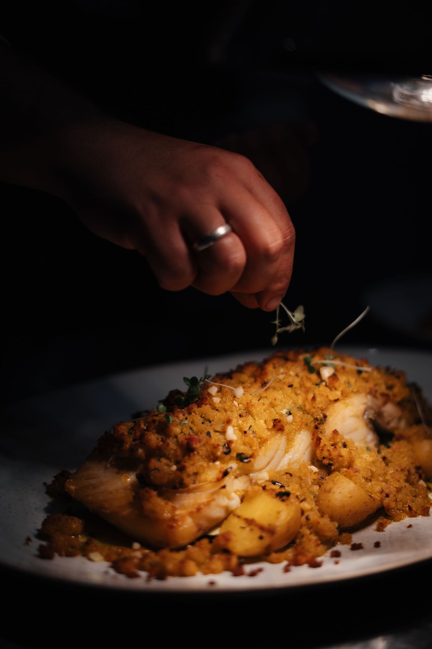 Chef garnishing a creamy pasta dish with herbs in dramatic lighting.