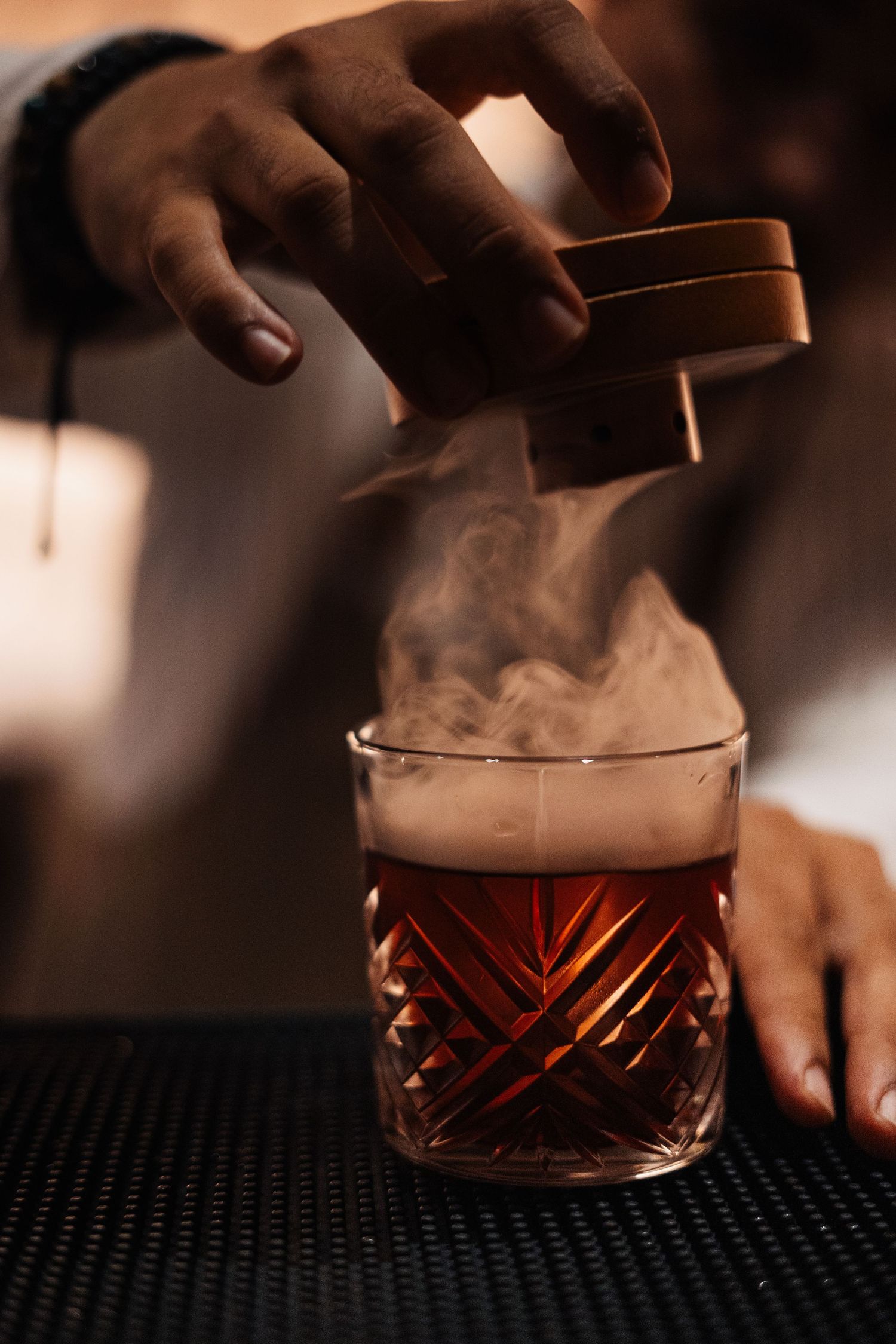 Smoky cocktail being prepared in an elegant cut crystal glass on a dark bar.
