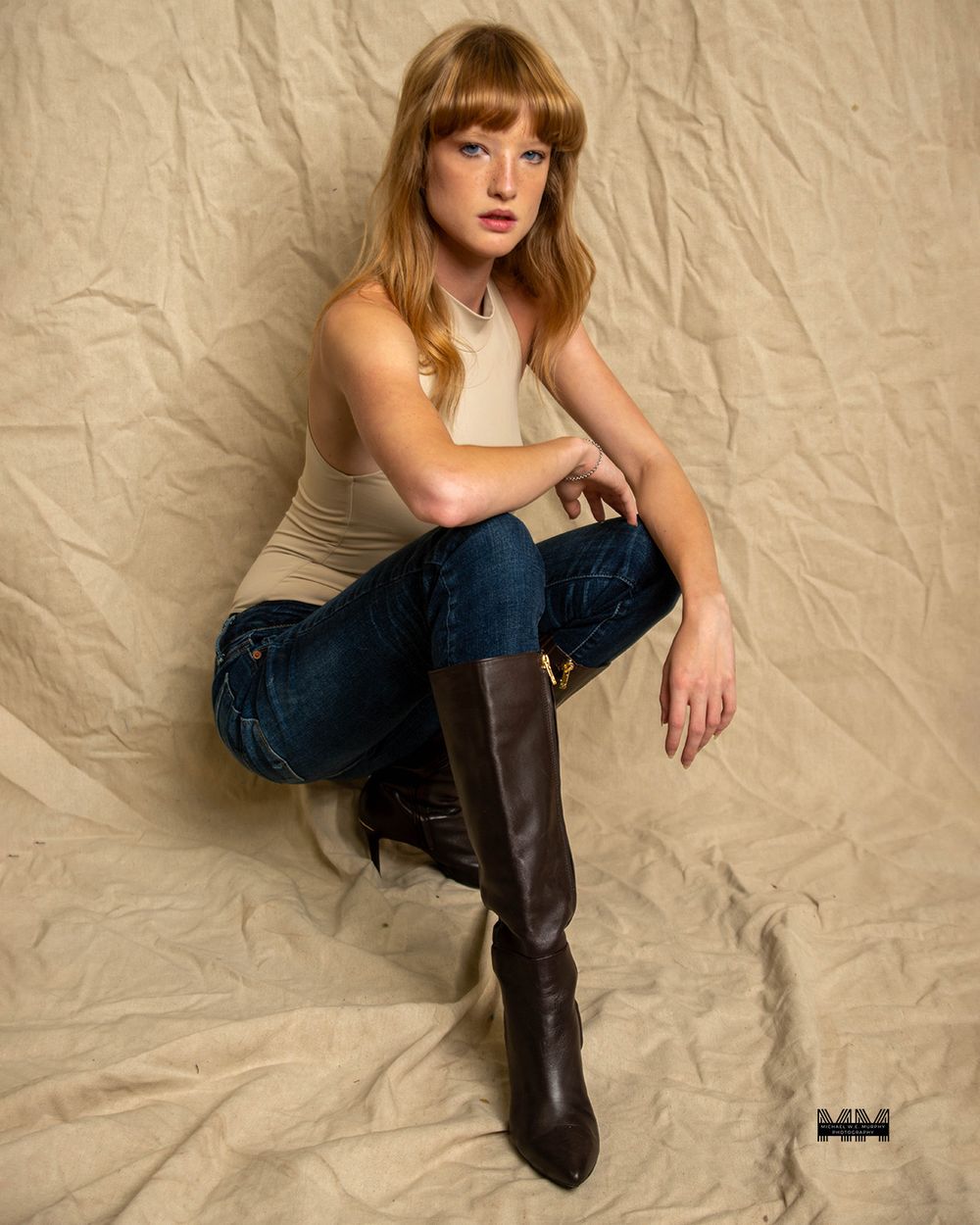 Fashion model in casual attire poses against textured beige backdrop in artistic photo series.