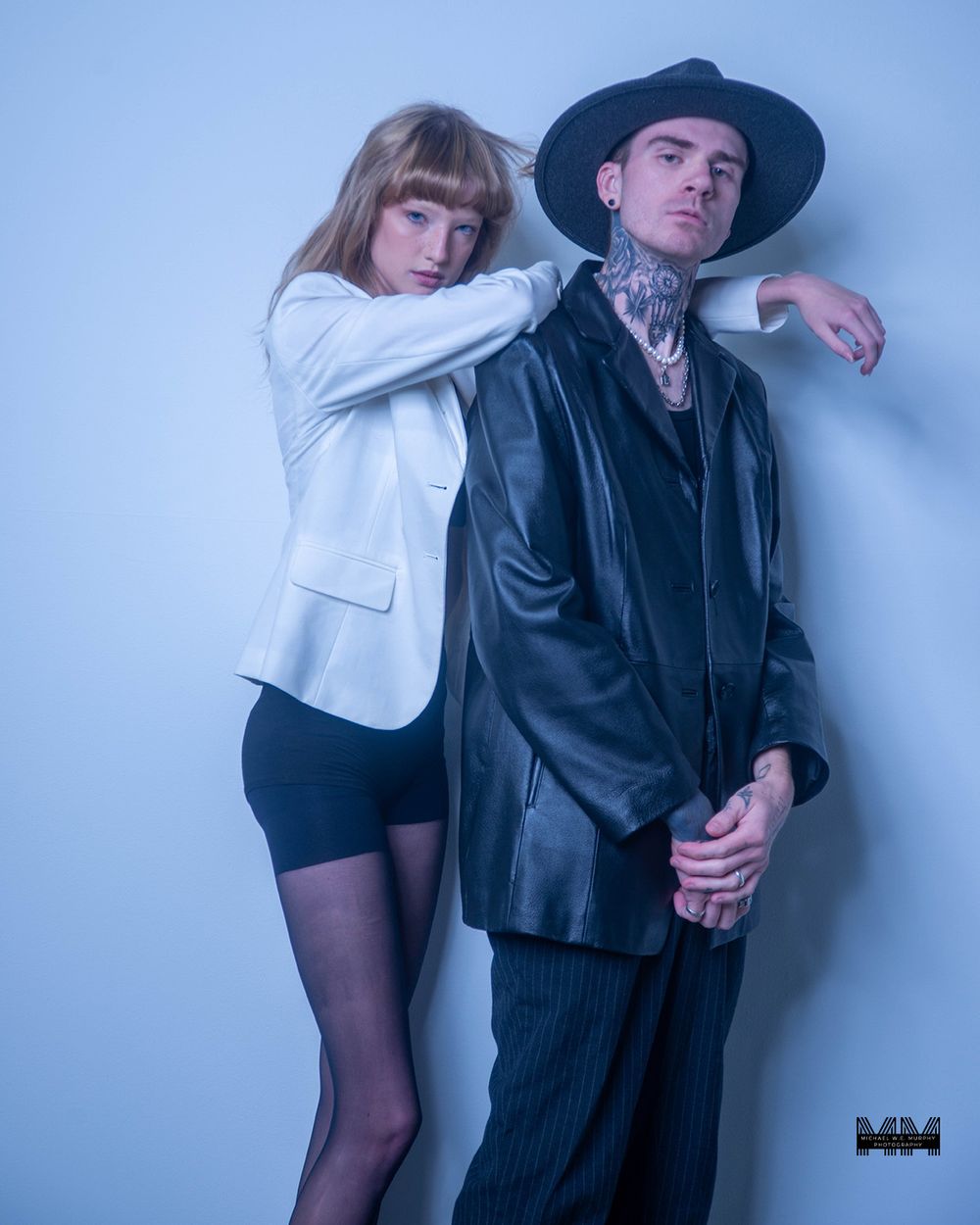Two people pose together against a blue wall in contrasting black and white outfits.