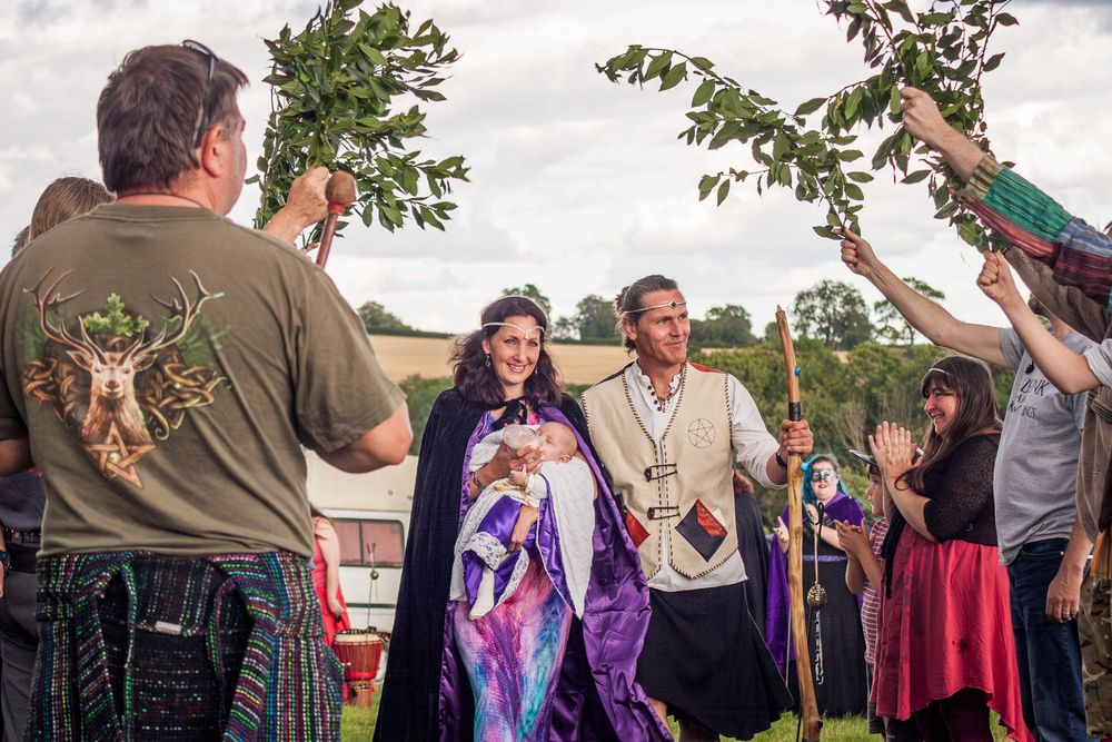 Mother, Father and baby leaving an outdoor pagan baby naming through an arch created by people holding up leafy branches.
