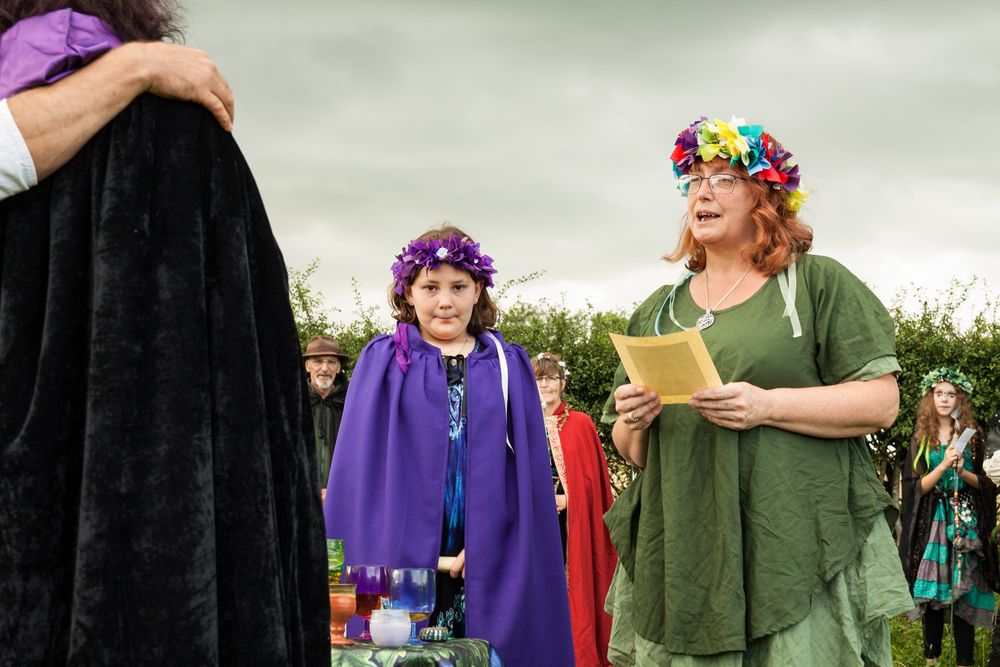 A high priestess in green, conducting a baby naming ceremony out in the countryside.