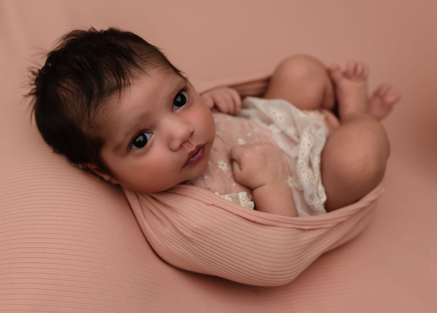 Awake newborn baby girl in pink lace dress wrapped in pink, posed on pink fabric at Charlottesville photography studio.