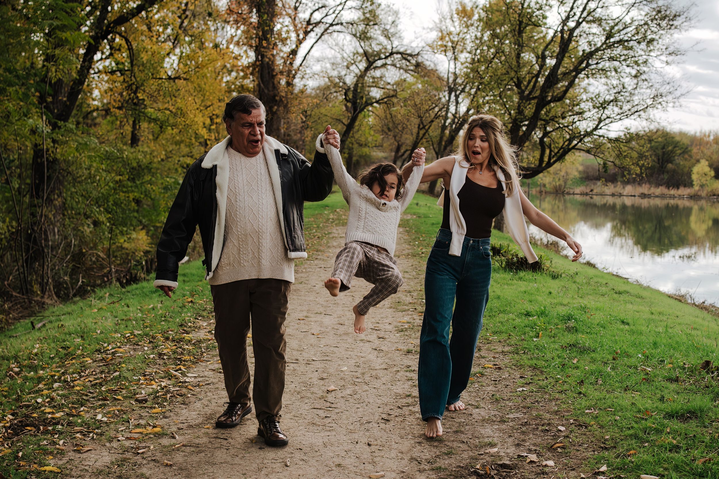 A joyful moment on a riverside path as a child jumps while holding hands with adults.