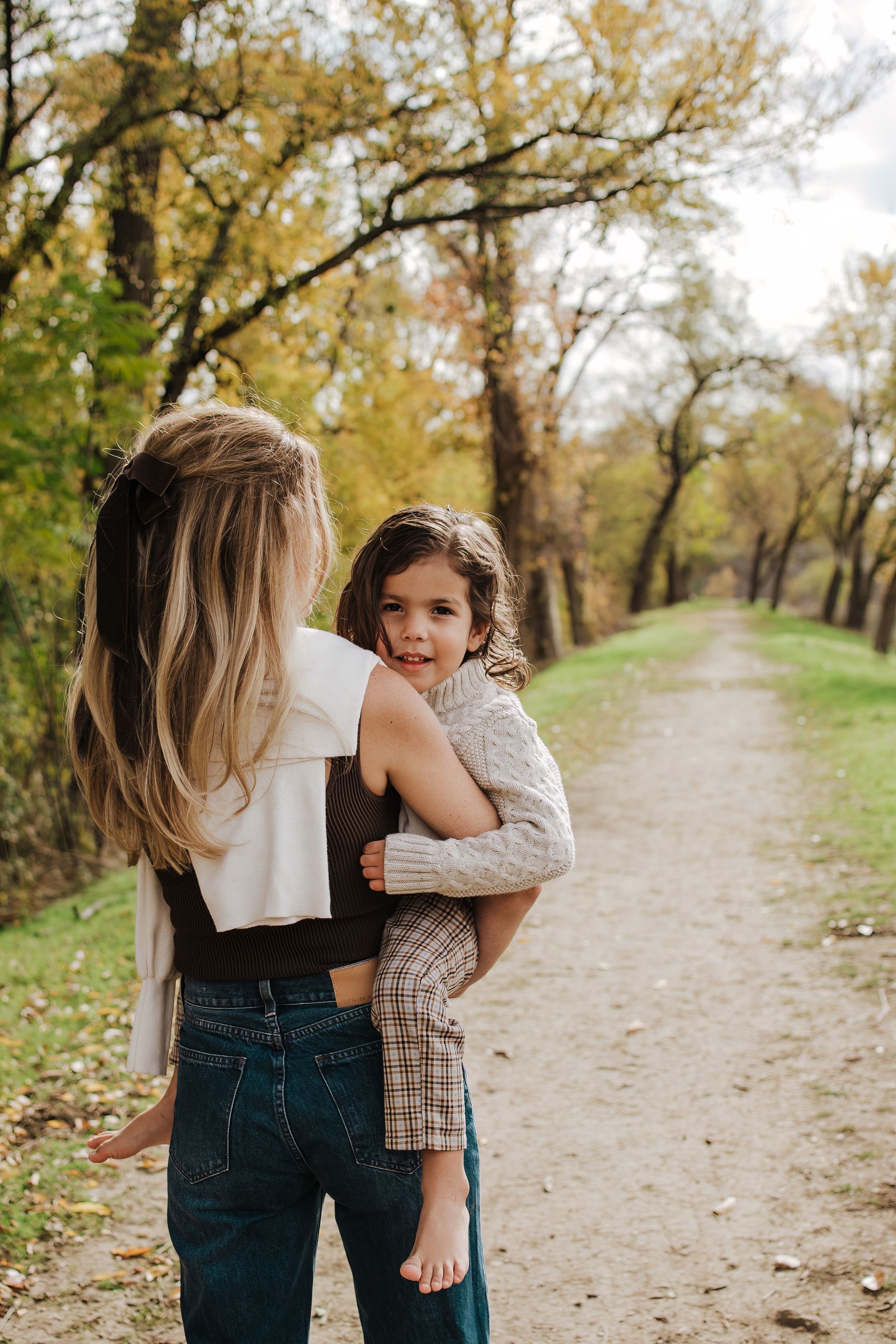 A family sharing a playful moment together on an autumn path lined with golden trees.