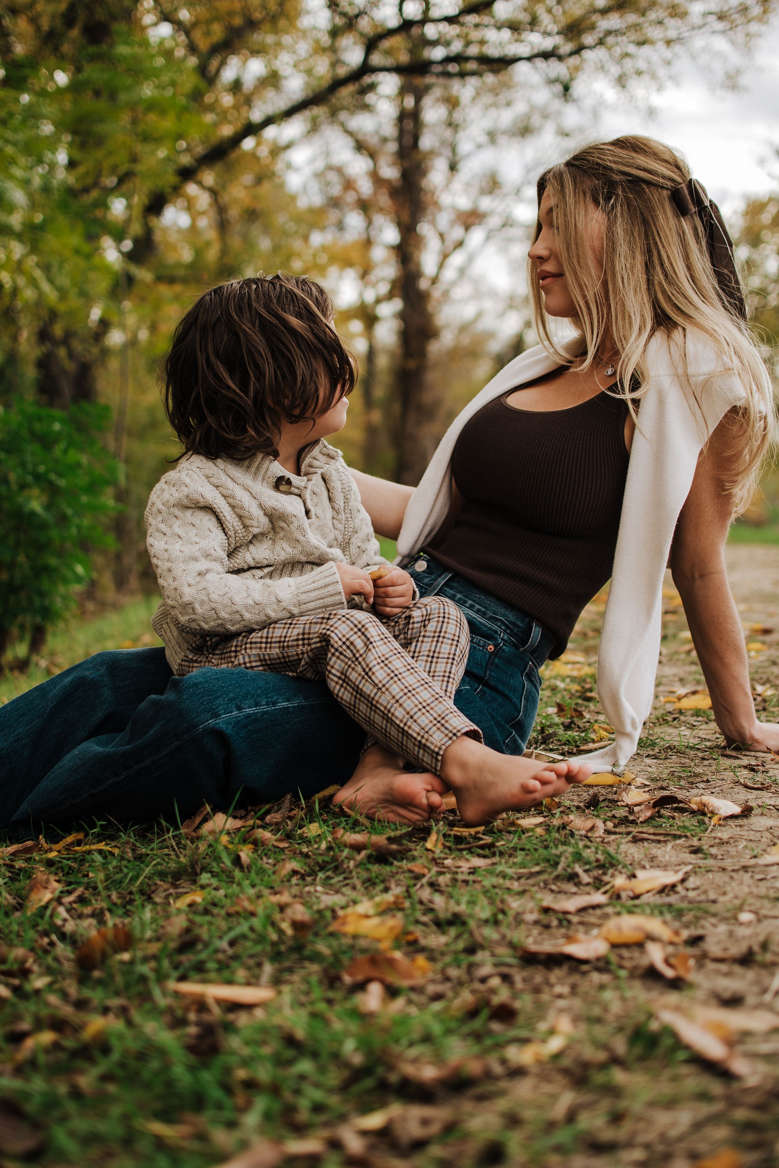 Family members relaxing together on fallen autumn leaves by a lakeside path.