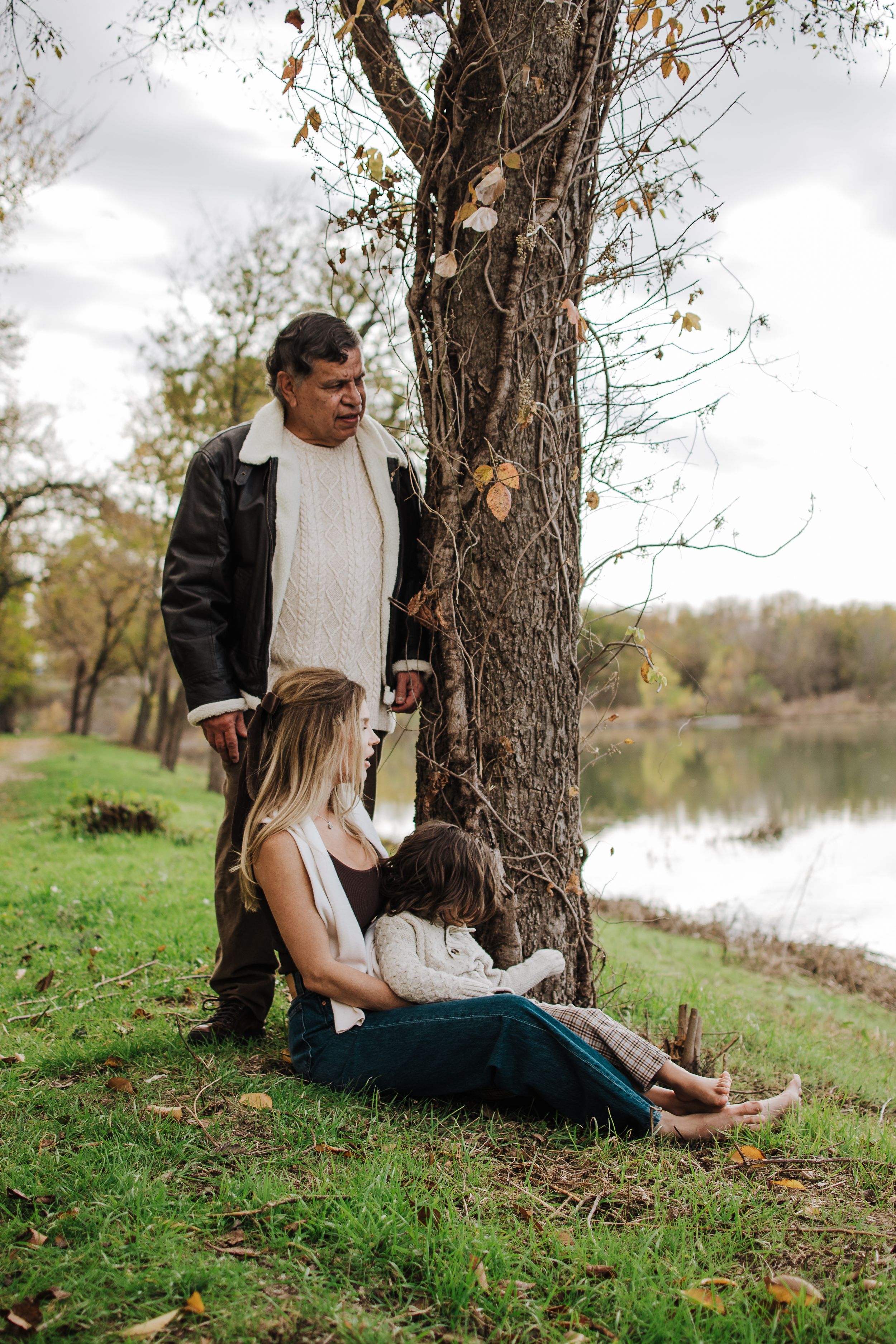 Family enjoying a peaceful moment together under trees by a serene lake.