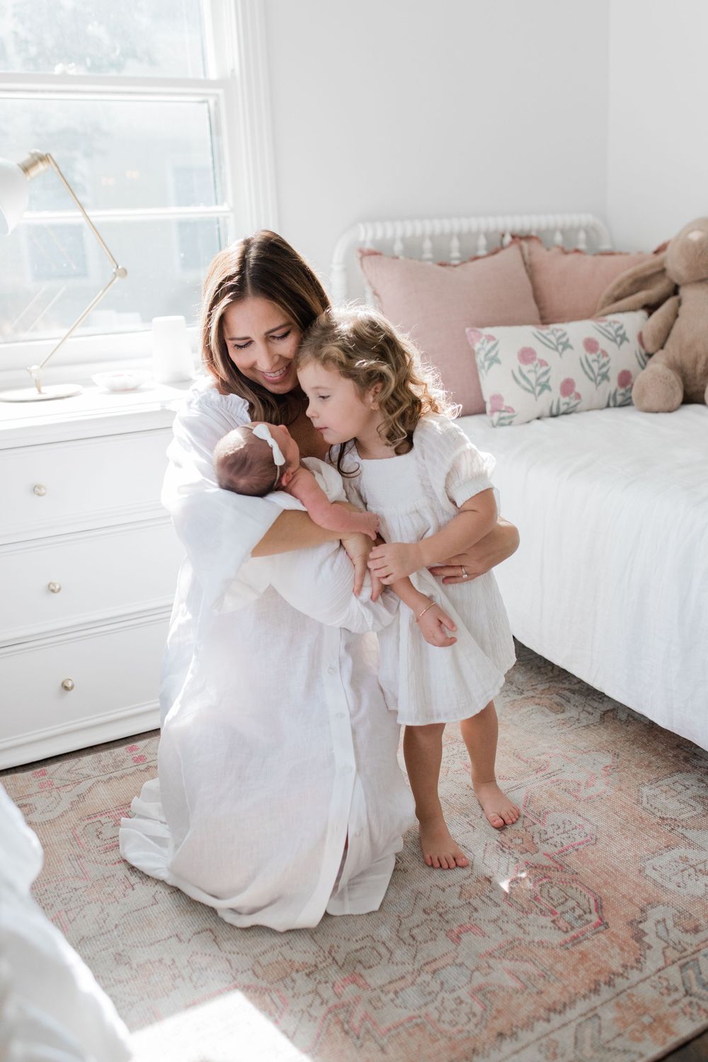 Tender family moments captured in soft white tones on ornate area rug in bright, airy room with natural lighting.