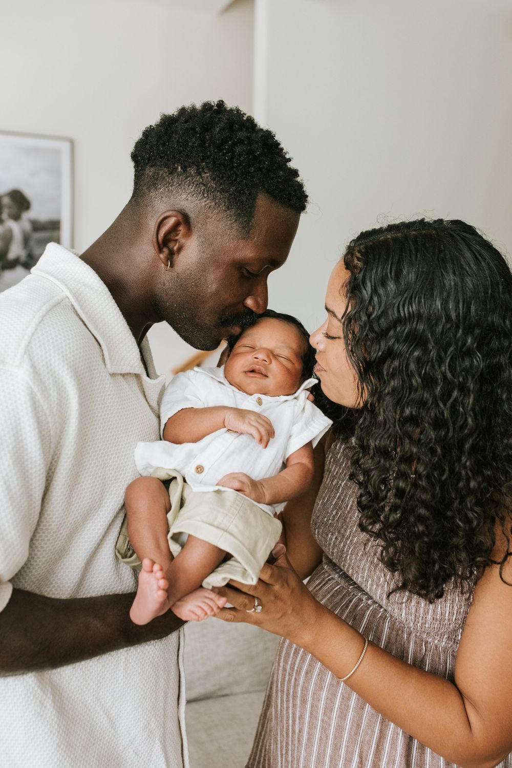 Parents lovingly hold and gaze at their newborn baby dressed in white while sharing an intimate family moment together.