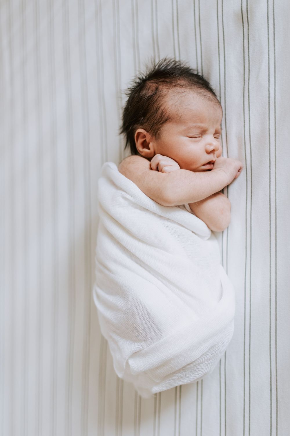 A sleeping newborn baby swaddled in white cloth shown from three angles against a white striped background.