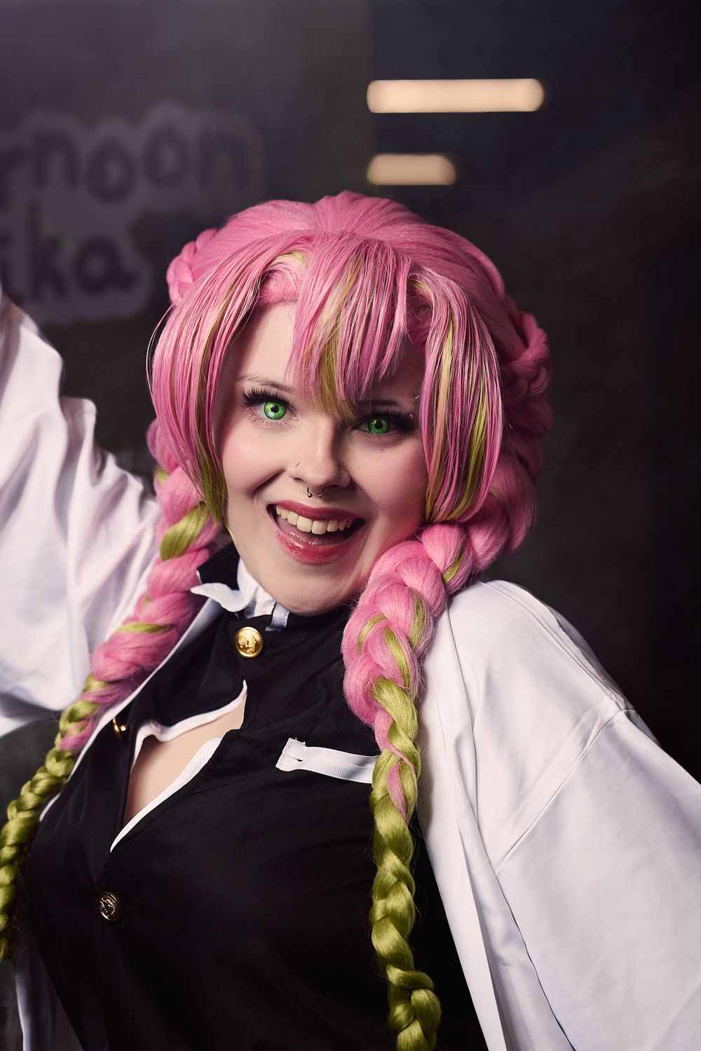 Cosplayer wearing pink and green braided wig with dramatic makeup poses in black and white outfit at convention.