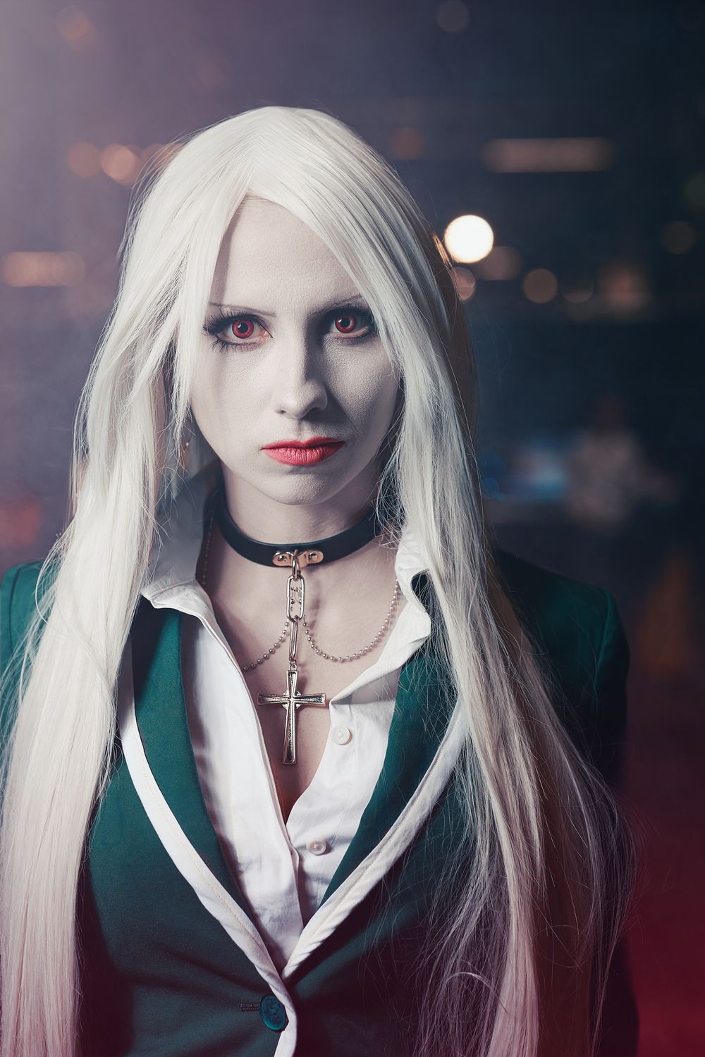 Gothic style portrait with long white hair, dark makeup, cross necklace and green blazer in moody lighting.