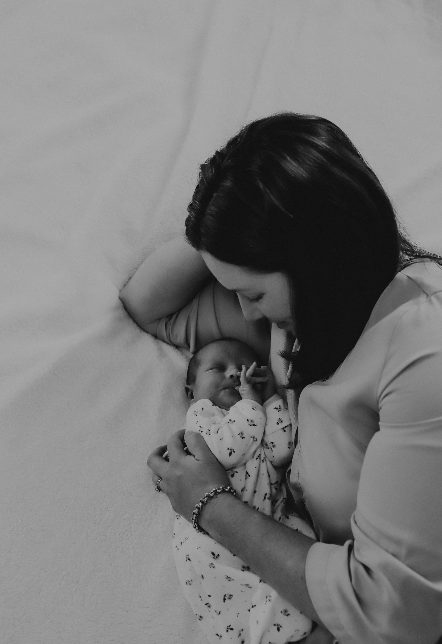 A tender black and white photo sequence showing a person lying in bed with a baby sharing an intimate snuggle moment.