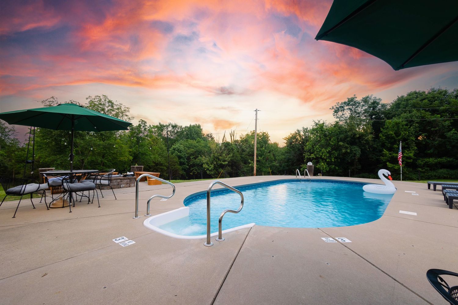 Luxurious curved swimming pool glowing at sunset with vibrant pink and orange sky reflecting in the calm water.