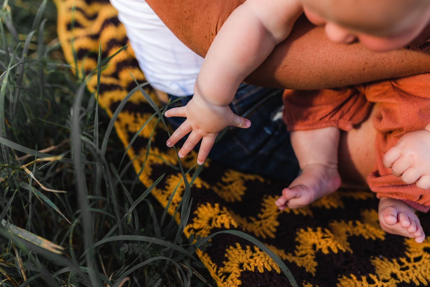 Small bare feet of a baby resting on an autumn-colored knit blanket in the grass.