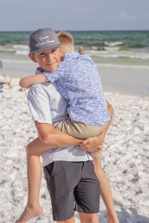Family embracing on white sandy beach with ocean waves in background.
