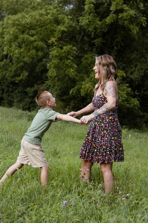 A playful scene in a grassy field shows two people chasing each other against a backdrop of green trees.