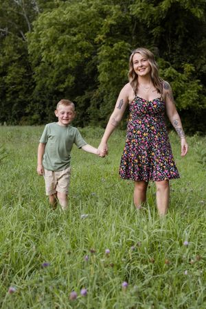 Two people run and laugh together through tall grass in a sunny outdoor setting.
