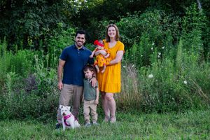 A white dog stands in the foreground while a family poses in the grassy background.