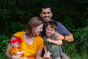 A family photo session in a lush green outdoor setting with warm yellow and orange clothing.