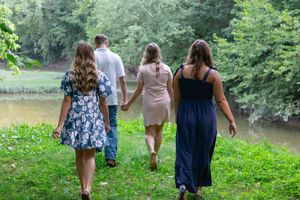 People walking together along a scenic path with green foliage and a pond in the background.