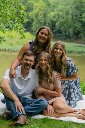 A casual group lounges on a white blanket near a pond during a summer photo session.