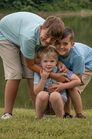 Three brothers in matching outfits share a playful group hug by a lake.