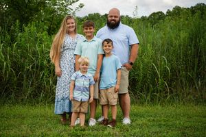 A family of five wearing coordinated blue and khaki outfits poses together in a grassy field.