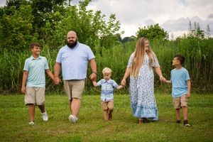 A family walks together holding hands through a green summer meadow.