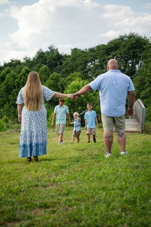 A family holds hands while walking through a green field on a summer day.