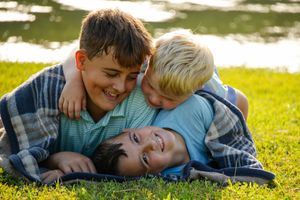 Family lying together on grass near water during golden hour outdoor photoshoot.