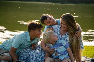 Family members sharing intimate moments during outdoor photo session near water.