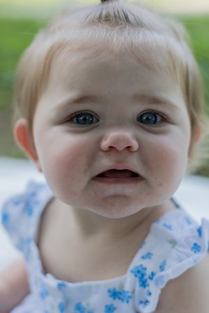 Close up portrait of baby wearing blue and white floral dress outdoors.