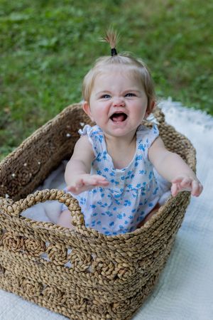 Happy baby sitting in woven basket on white blanket outdoors.
