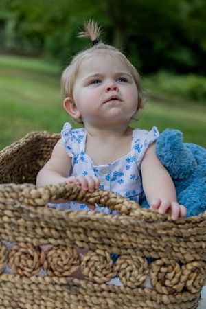 Baby peering over edge of woven basket with blue plush toy.
