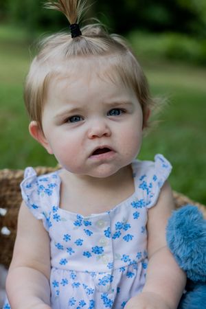 Baby with tiny ponytail wearing blue floral dress sitting outdoors.
