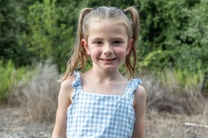Young girl in blue and white gingham dress smiling outdoors.