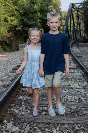 Two children walking together on railroad tracks wearing coordinated outfits.